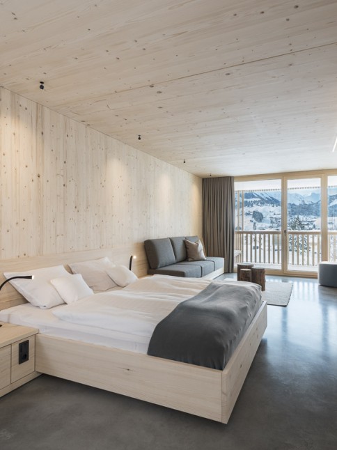 Schlichtes Hotelzimmer mit Holzwänden, Sichtbeton und grauen Vorhängen im 4 Sterne Hotel Oswalda Hus im Kleinwalsertal.